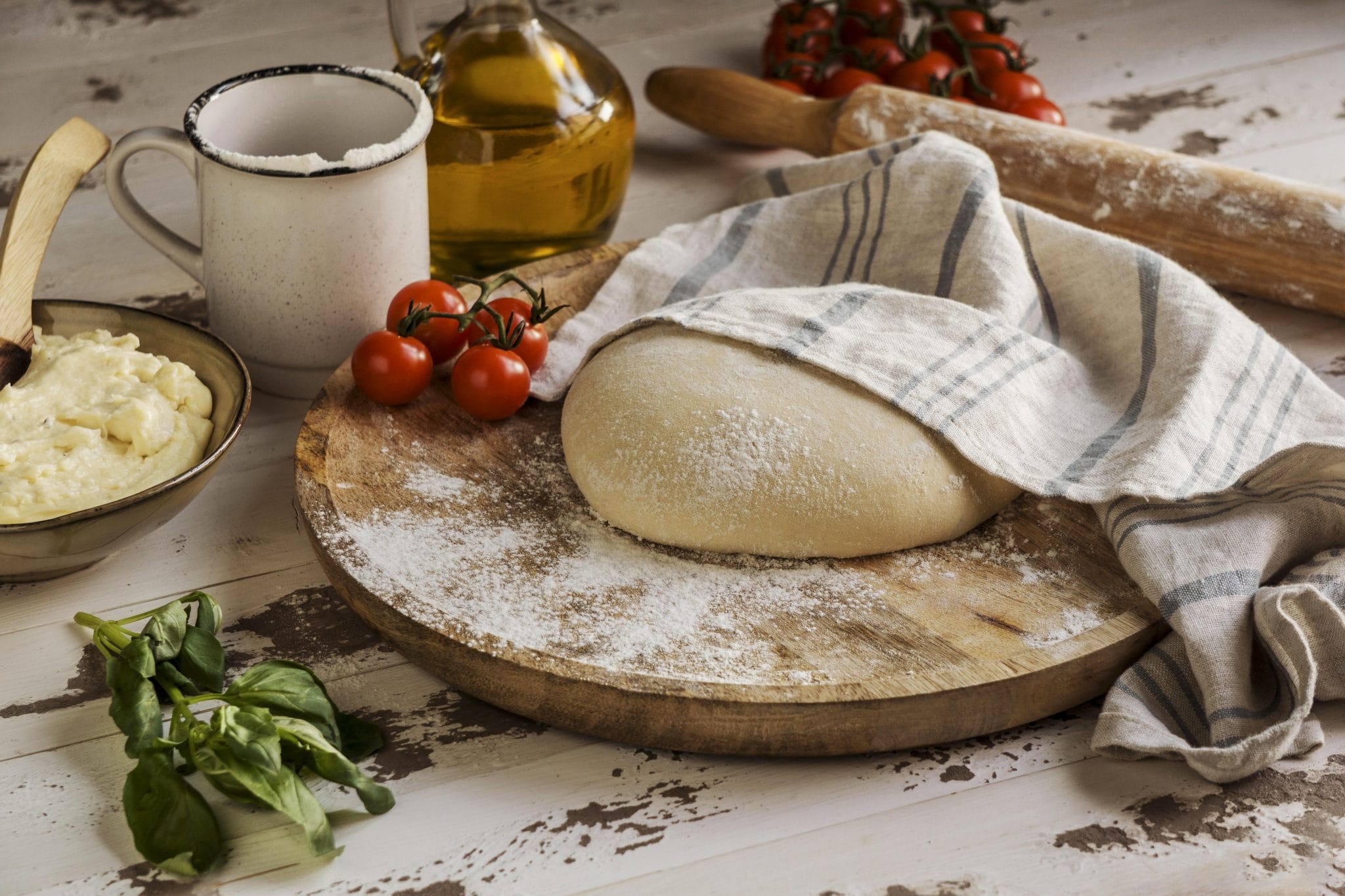 Pizza Dough Covered With Cloth Next To Oil And Tomatoes Scaled