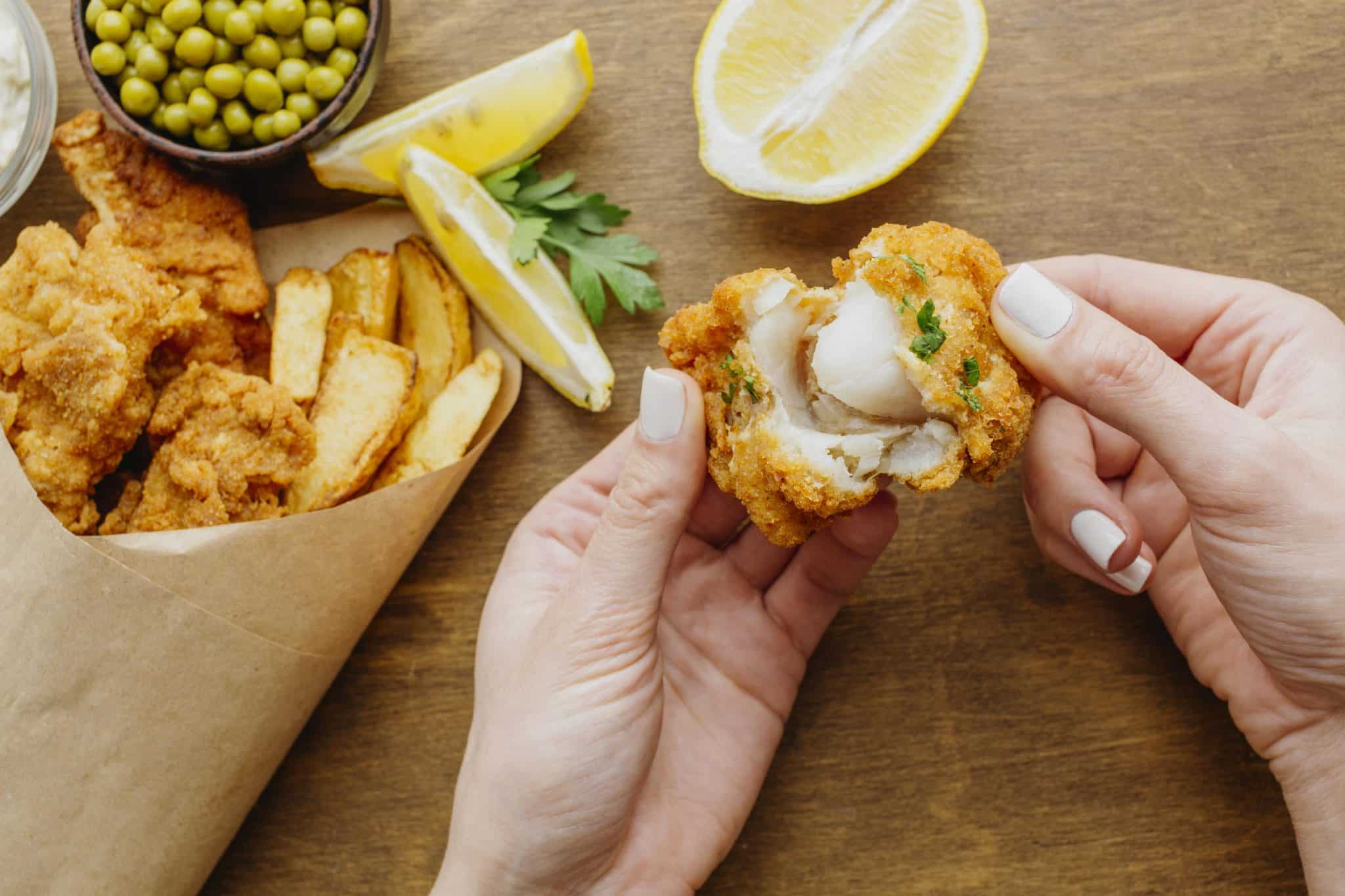 Top View Fish Chips Paper Wrap With Woman Breaking Piece Scaled